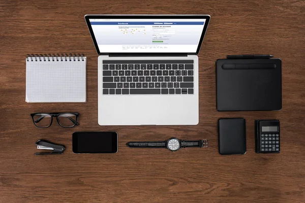 Vista superior del lugar de trabajo con libro de texto vacío arreglado, teléfono inteligente, reloj de pulsera y portátil con facebook en la pantalla - foto de stock