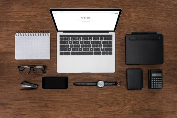 Top view of workplace with arranged empty textbook, smartphone, wristwatch and laptop with google on screen — Stock Photo