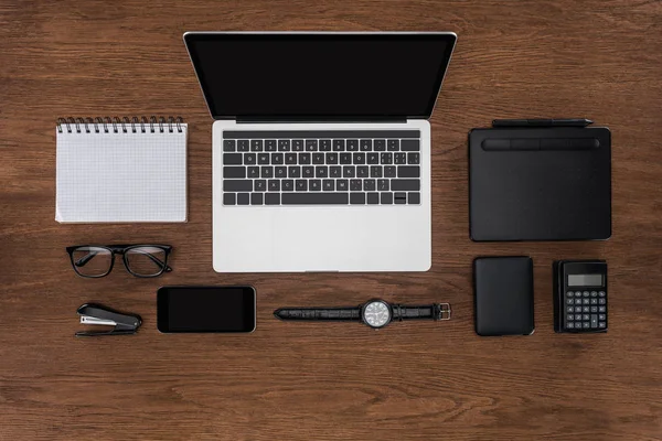 Top view of workplace with arranged empty textbook, smartphone, wristwatch and laptop with blank screen — Stock Photo