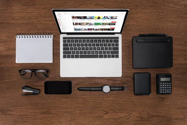 Vista dall'alto del posto di lavoro con libro di testo vuoto organizzato, smartphone, orologio da polso e laptop con youtube sullo schermo — Foto stock