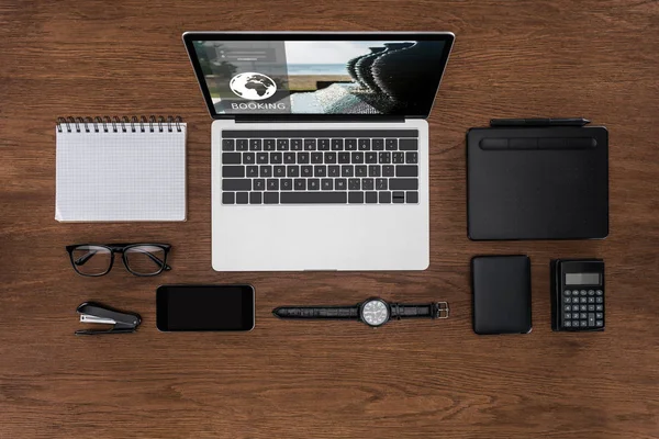 Top view of workplace with arranged empty textbook, smartphone, wristwatch and laptop with booking on screen — Stock Photo