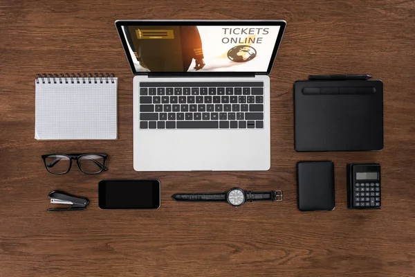 Vista dall'alto del posto di lavoro con libro di testo vuoto organizzato, smartphone, orologio da polso e laptop con biglietti online sullo schermo — Foto stock