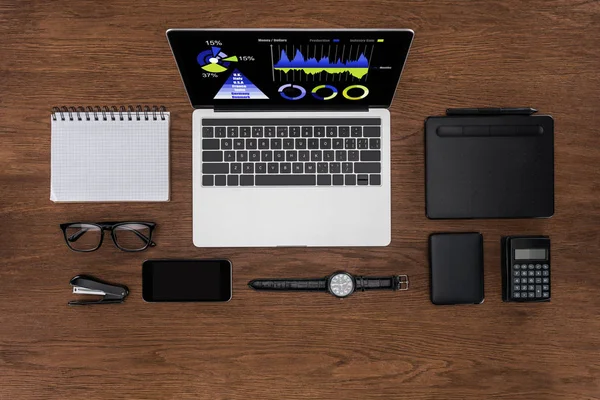 Vista dall'alto del posto di lavoro con libro di testo vuoto organizzato, smartphone, orologio da polso e laptop con grafica sullo schermo — Foto stock