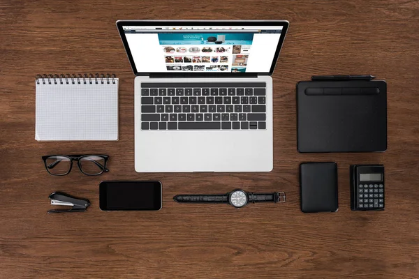 Вид сверху на рабочее место с устроенным пустым учебником, смартфоном, наручными часами и ноутбуком с Amazon на экране — стоковое фото