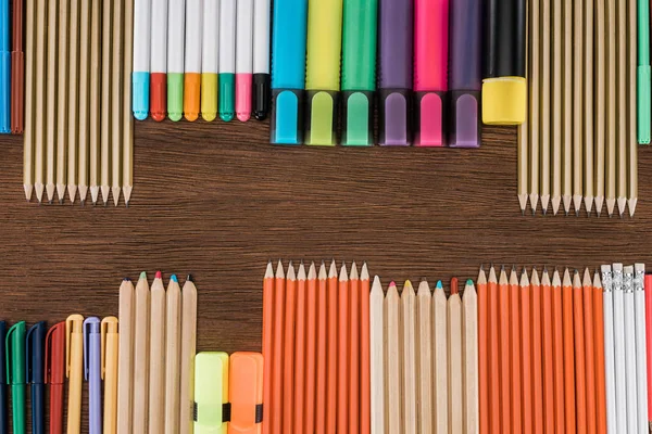 Tendido plano con lápices y marcadores de colores dispuestos en la mesa de madera - foto de stock