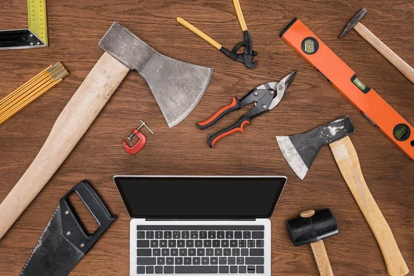 Top view of laptop with blank screen surrounded by various tools on wooden table — Stock Photo