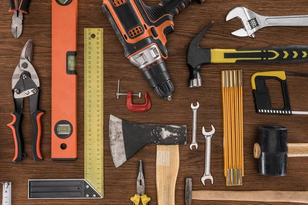 Vue de dessus de hache, perceuse électrique, niveau d'esprit, marteaux et divers outils sur table en bois — Photo de stock