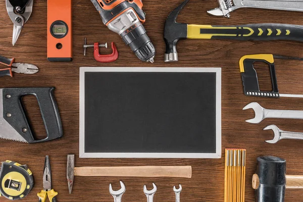 Vue de dessus du tableau noir vide près des divers outils disposés sur la table en bois — Photo de stock