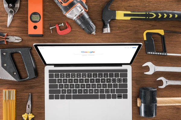 Vista dall'alto del posto di lavoro con computer portatile con google sullo schermo circondato da vari strumenti su tavolo in legno — Foto stock