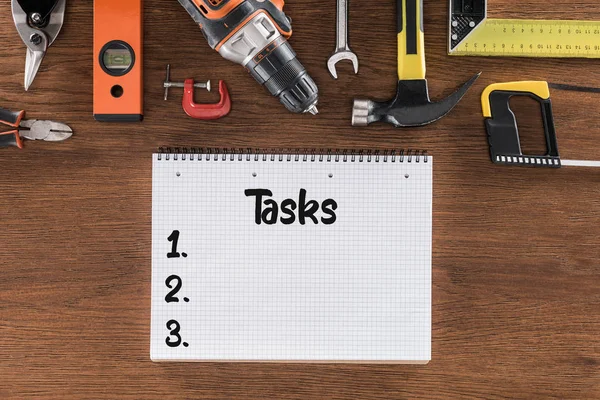 Vista superior del libro de texto con tareas de escritura cerca de varias herramientas en la mesa de madera - foto de stock