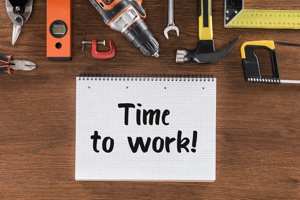 Vista superior del libro de texto con tiempo de escritura para trabajar cerca de varias herramientas en la mesa de madera - foto de stock