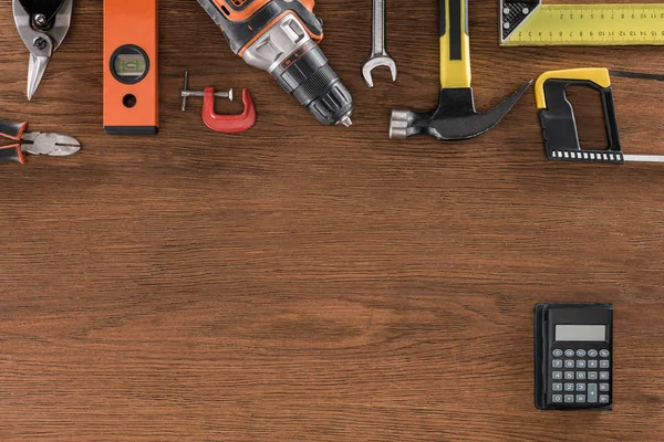 Vue de dessus de divers outils disposés et calculatrice sur table en bois — Photo de stock
