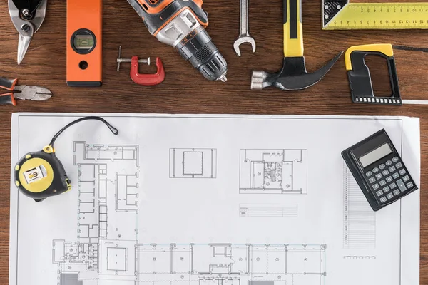 Top view of architect blueprint, tape measurement, calculator and various tools on wooden table — Stock Photo