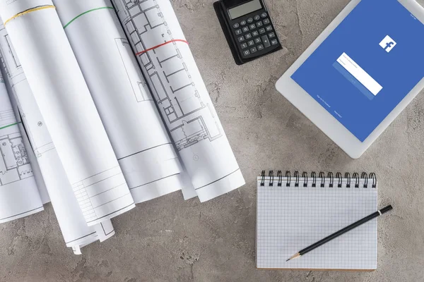 Ansicht des Architekten-Arbeitsplatzes mit leerem Lehrbuch, Taschenrechner und digitalem Tablet mit Facebook auf dem Bildschirm — Stockfoto