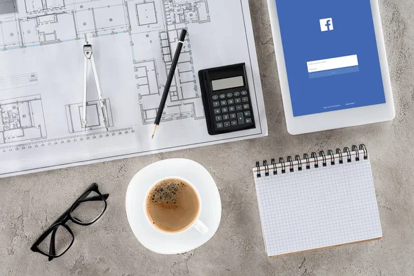 Vue de dessus du lieu de travail de l'architecte avec plan, diviseur, café et tablette numérique avec facebook à l'écran — Photo de stock