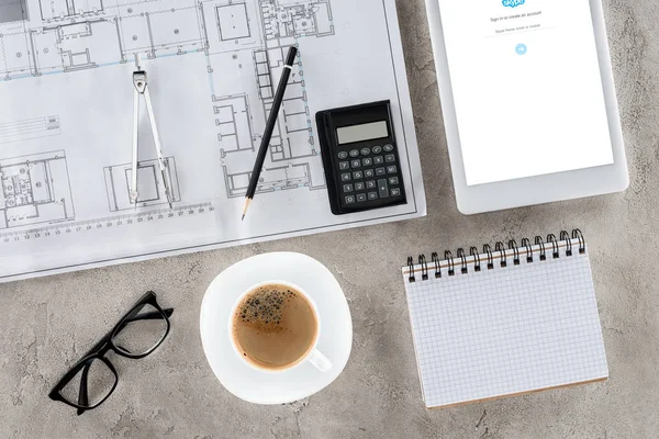 Vista dall'alto del luogo di lavoro dell'architetto con cianografia, divisore, caffè e tablet digitale con skype sullo schermo — Foto stock