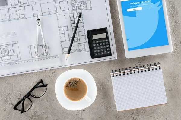 Vue de dessus du lieu de travail de l'architecte avec plan, diviseur, café et tablette numérique avec twitter à l'écran — Photo de stock