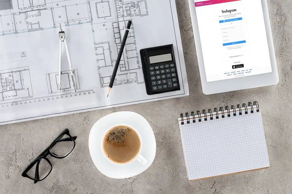 Ansicht des Architekten-Arbeitsplatzes mit Blaupause, Trennwand, Kaffee und digitalem Tablet mit Instagram auf dem Bildschirm — Stockfoto