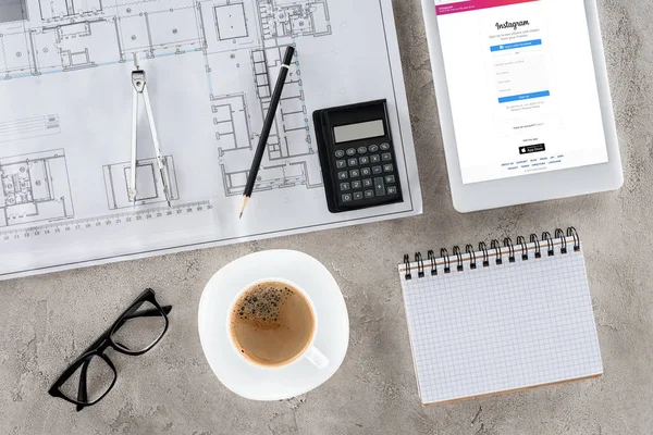 Vue de dessus du lieu de travail de l'architecte avec plan, diviseur, café et tablette numérique avec instagram à l'écran — Photo de stock