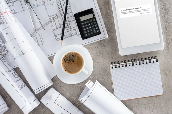 Ansicht des Architekten-Arbeitsplatzes mit Kaffeetasse, Blaupausen, Taschenrechner und digitalem Tablet mit blockierter Seite von vk.com auf dem Bildschirm — Stockfoto