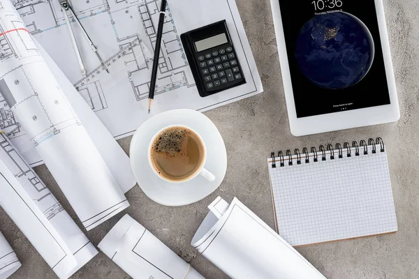 Вид на рабочее место архитектора с чашкой кофе, чертежами, калькулятором и планшетом ipad на столе — стоковое фото