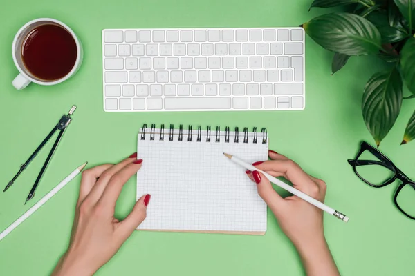 Image recadrée de femme architecte écrivant dans un manuel vide à la table avec clavier d'ordinateur, diviseur et tasse à café — Photo de stock