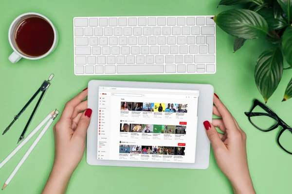 Image recadrée de femme architecte tenant tablette numérique avec youtube à l'écran à la table avec diviseur, café et plante en pot — Photo de stock