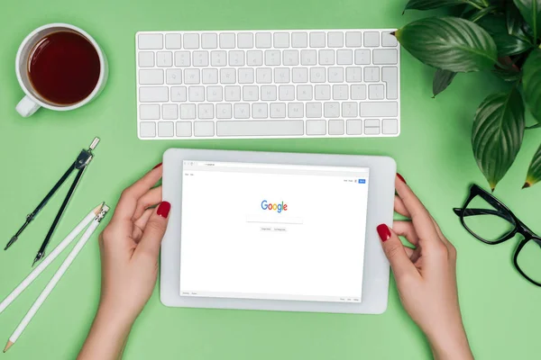 Cropped image of female architect holding digital tablet with google on screen at table with divider, coffee and potted plant — Stock Photo