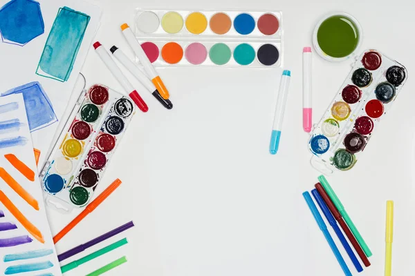 Вид зверху на робоче місце художника з барвистими фарбами та маркерами на білому столі — стокове фото