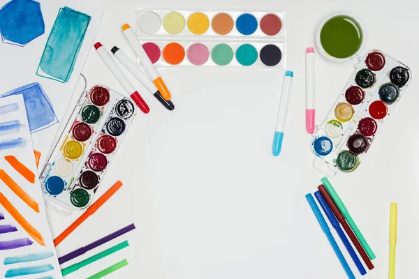 Vue de dessus du lieu de travail de l'artiste avec des peintures colorées et des marqueurs sur la table blanche — Photo de stock