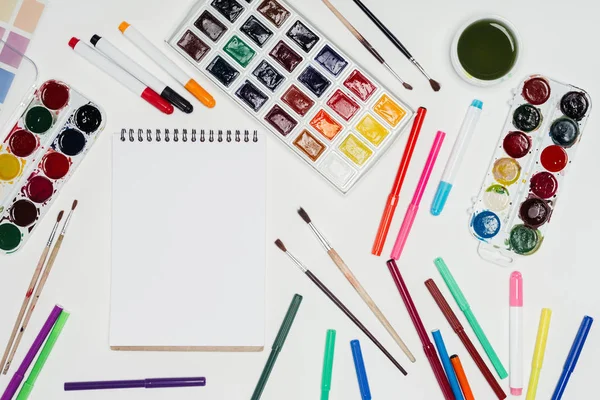 Top view of artist workplace with empty textbook, paintbrushes, colorful paints and markers — Stock Photo