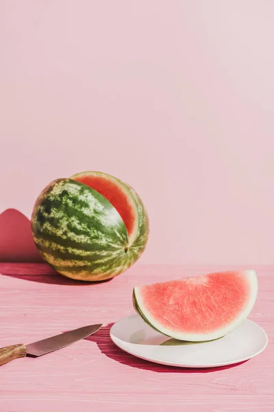 Nahaufnahme einer Scheibe Wassermelone auf Teller und Messer auf rosa Hintergrund — Stockfoto