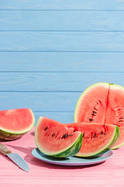 Nahaufnahme von Wassermelonenstücken und Messer auf rosa Tischplatte auf blauem Hintergrund — Stockfoto