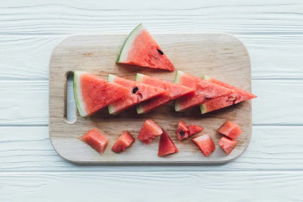 Flache Lage mit angeordneten Wassermelonenstücken auf Schneidebrett auf Holztischplatte — Stockfoto