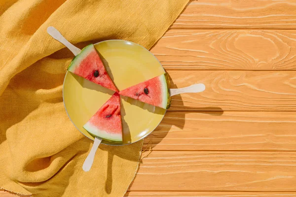 Flat lay with watermelons on ice cream sticks on plate on wooden tabletop with linen — Stock Photo