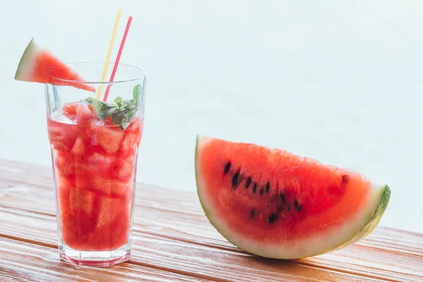 Vista de perto da refrescante bebida de melancia com hortelã em vidro e fatia na melancia na superfície de madeira — Fotografia de Stock