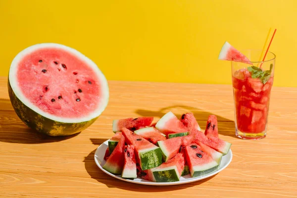 Nahaufnahme von frischen Wassermelonenstücken und Wassermelonengetränk im Glas auf Holzoberfläche auf gelbem Hintergrund — Stockfoto