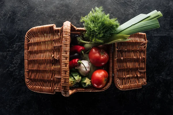 Flat lay with various fresh vegetables in basket on black marble tabletop — Stock Photo