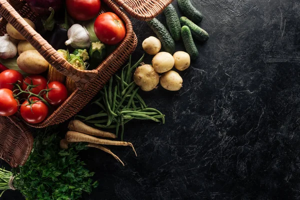 Flat lay with various fresh vegetables in basket on black marble tabletop — Stock Photo