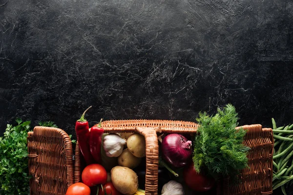 Flat lay with various fresh vegetables in basket on black marble tabletop — Stock Photo