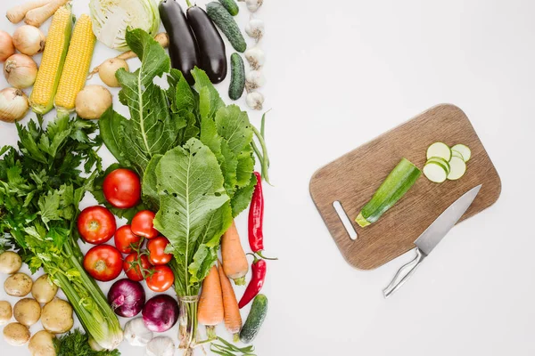 Vue du dessus des légumes mûrs et planche à découper avec couteau et courgettes coupées isolées sur blanc — Photo de stock