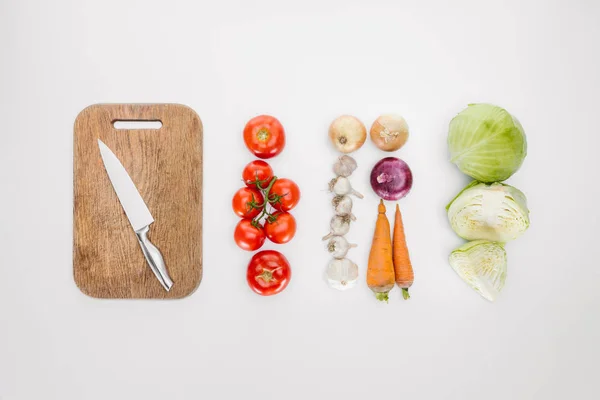 Top view of arranged ripe vegetables and cutting board with knife isolated on white — Stock Photo