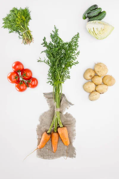 Flat lay with carrots on sackcloth and vegetables arranged around isolated on white — Stock Photo