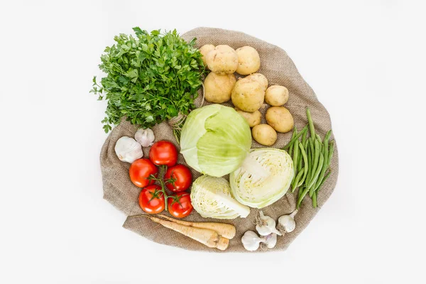 Food composition with fresh vegetables arranged on sackcloth isolated on white — Stock Photo