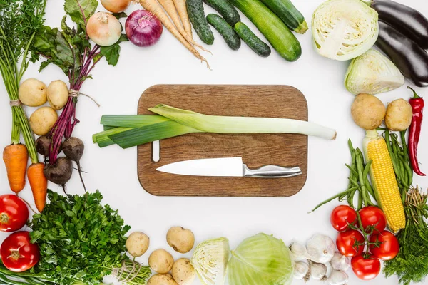 Vista superior de vegetais maduros e tábua de corte com faca e alho-porro isolado em branco — Fotografia de Stock