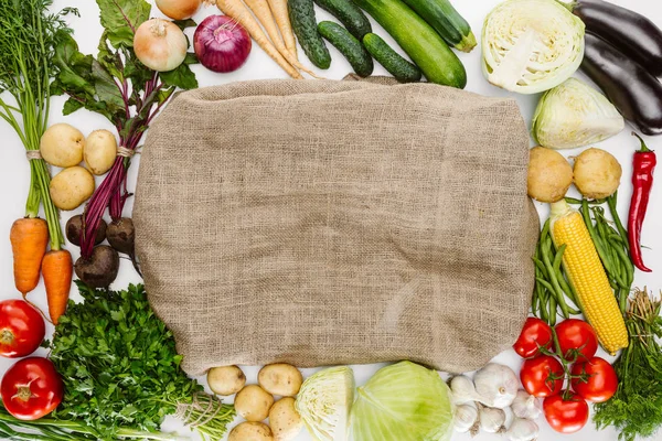 Composição de alimentos com vegetais maduros dispostos em torno de pano de saco isolado em branco — Fotografia de Stock