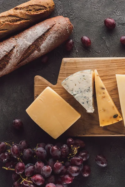 Acostado plano con baguettes, queso surtido y uva en la mesa oscura - foto de stock