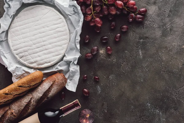 Flat lay with food composition of bread loafs, camembert cheese and bottle of wine on dark surface — Stock Photo