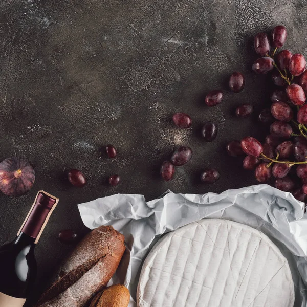 Flat lay with food composition of bread loafs, camembert cheese and bottle of wine on dark surface — Stock Photo