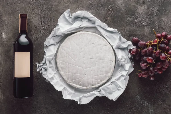 Top view of bottle of wine, brie cheese and grape on dark surface — Stock Photo